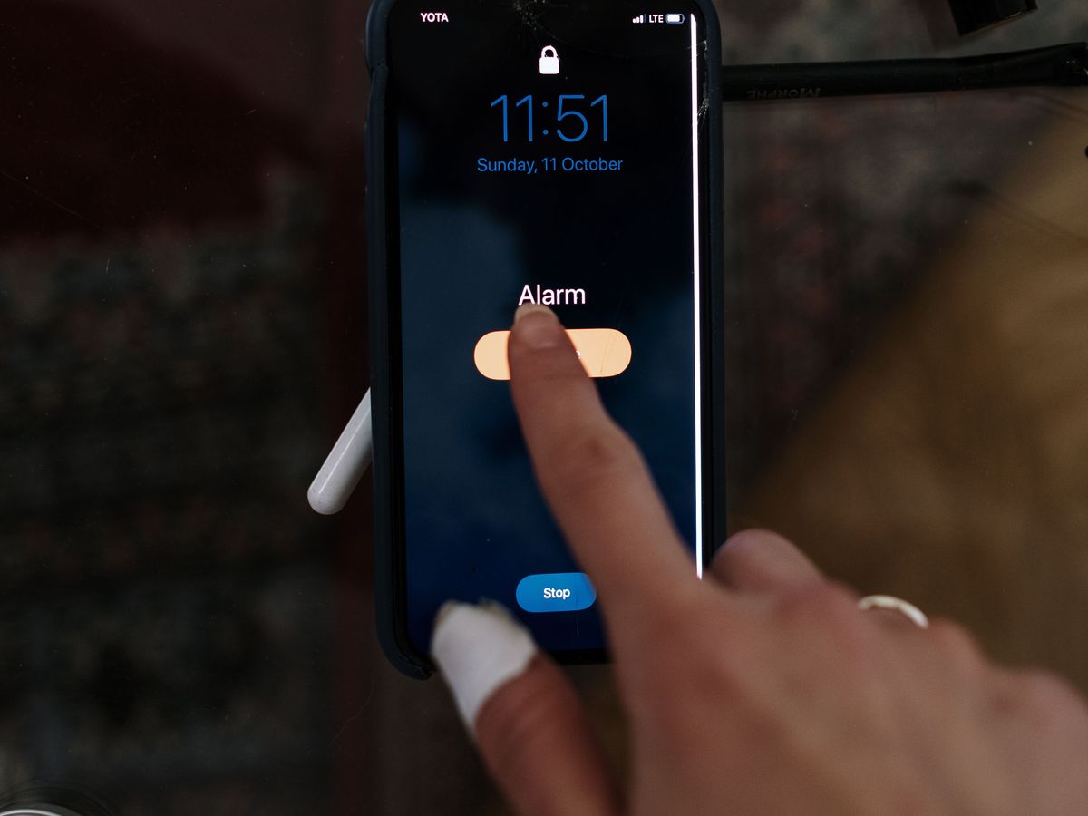 A finger pressing snooze on a ringing phone alarm