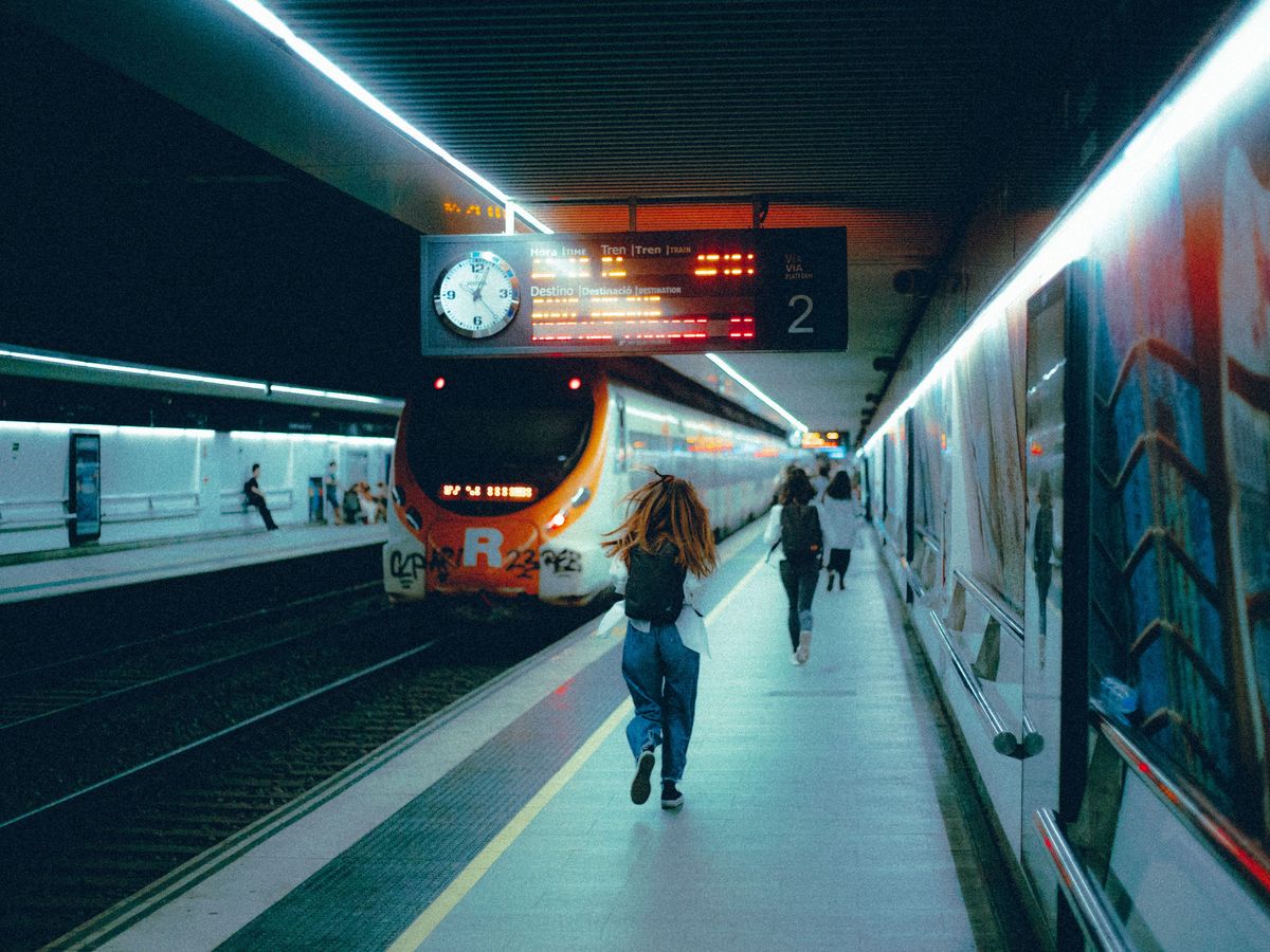 A young woman running along a station platform towards a departing train